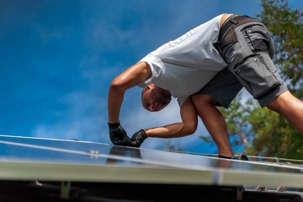 Man worker installing solar photovoltaic panels on a roof, alternative energy, saving resources and sustainable lifestyle concept.