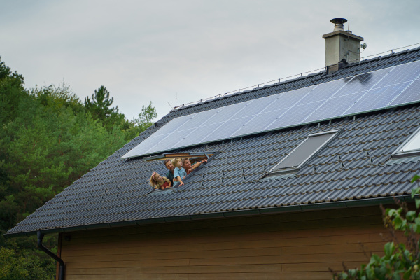 Happy family looking out from skylight window in their house with solar panels on the roof. Alternative energy, saving resources and sustainable lifestyle concept.