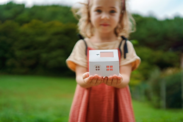 Close up of little girl holding paper model of house with the solar panels.Alternative energy, saving resources and sustainable lifestyle concept.