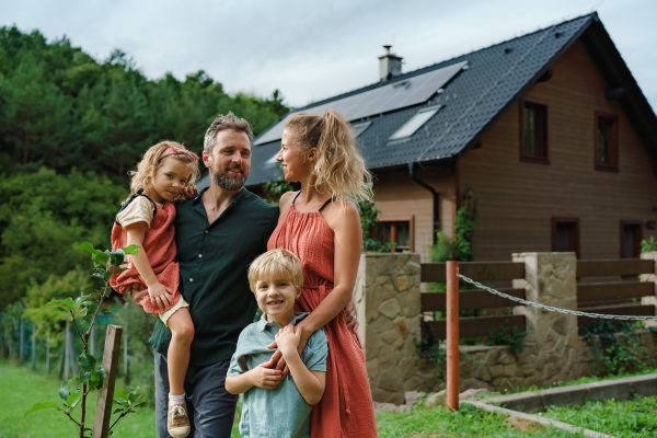 Happy family near their house with a solar panels. Alternative energy, saving resources and sustainable lifestyle concept.