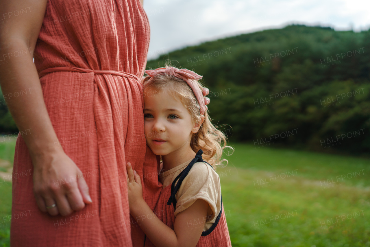 Little daughter leaning of her mother, enjoying together time outdoor at a meadow.