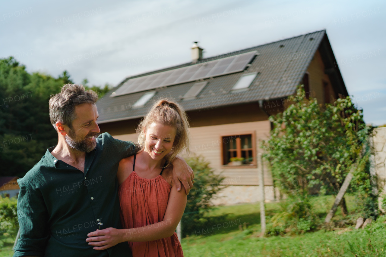 Happy couple standying near their house with a solar panels. Alternative energy, saving resources and sustainable lifestyle concept.