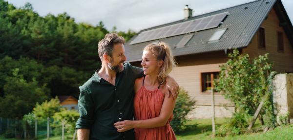 Happy couple standying near their house with a solar panels. Alternative energy, saving resources and sustainable lifestyle concept.