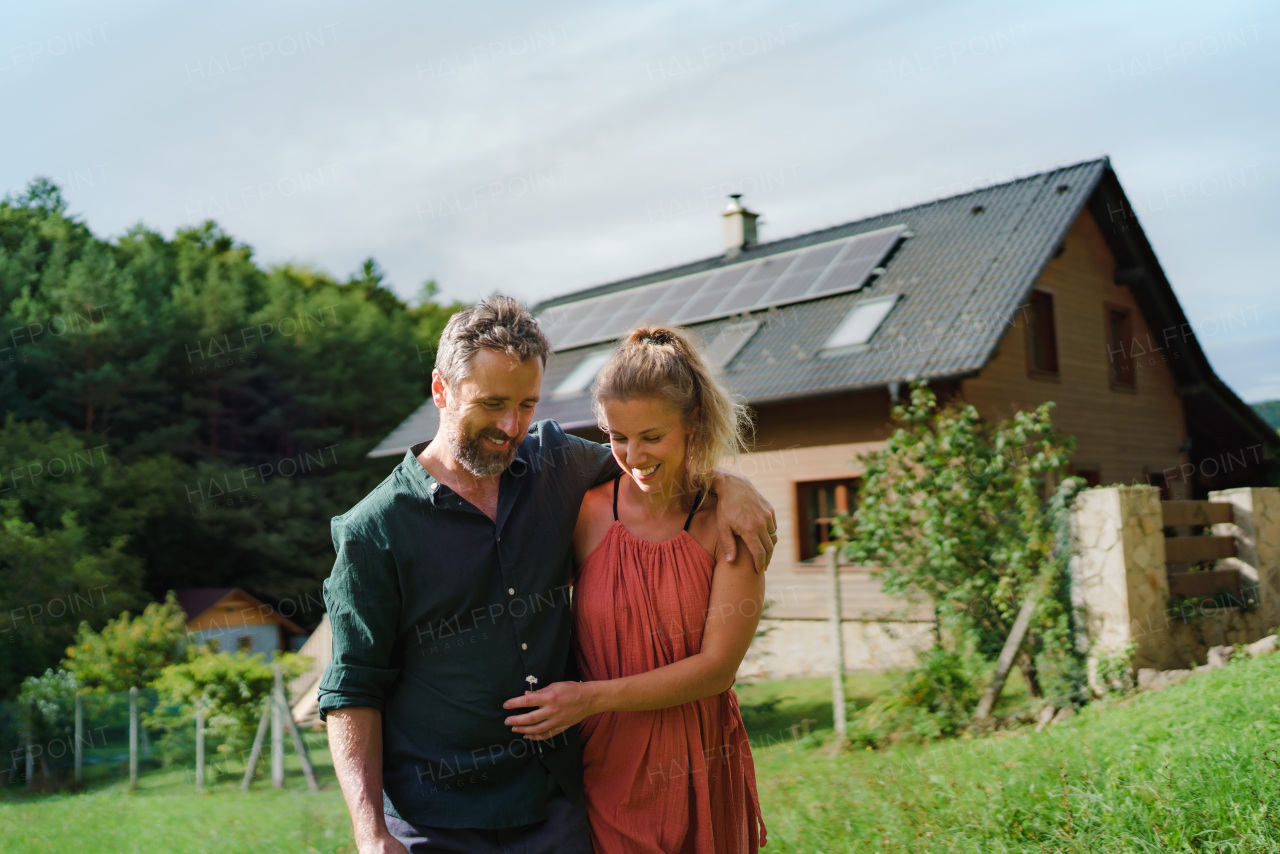 Happy couple standying near their house with a solar panels. Alternative energy, saving resources and sustainable lifestyle concept.