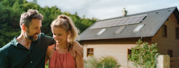 Happy couple standying near their house with a solar panels. Alternative energy, saving resources and sustainable lifestyle concept.