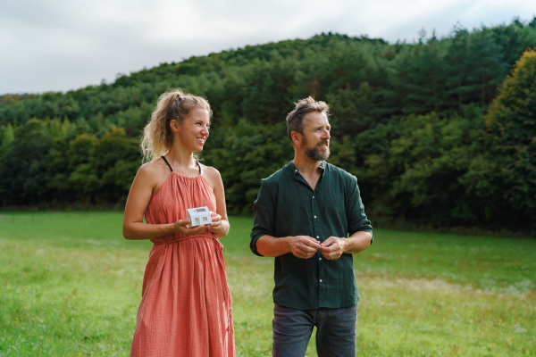 Close-up of happy couple holding paper model of house with solar panels, looking and dreaming about future. Alternative energy, saving resources and sustainable lifestyle concept.