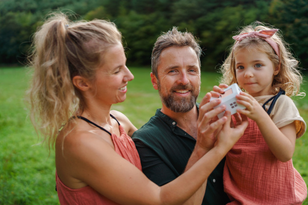 Little girl with her parents holding paper model of house with the solar panels.Alternative energy, saving resources and sustainable lifestyle concept.