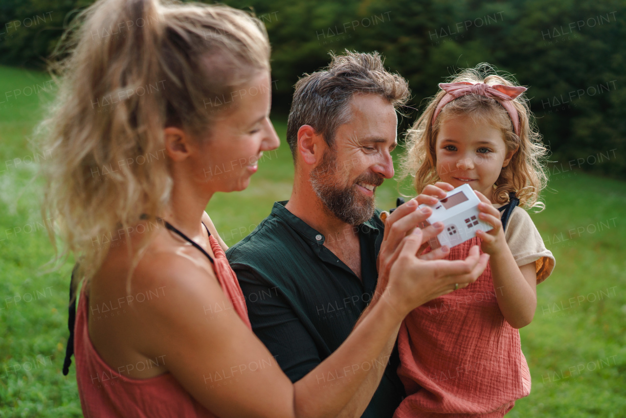 Little girl with her parents holding paper model of house with the solar panels.Alternative energy, saving resources and sustainable lifestyle concept.