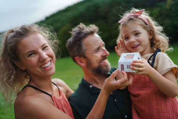 Little girl with her parents holding paper model of house with the solar panels.Alternative energy, saving resources and sustainable lifestyle concept.