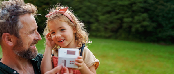 Little girl with her father holding paper model of house with the solar panels.Alternative energy, saving resources and sustainable lifestyle concept.