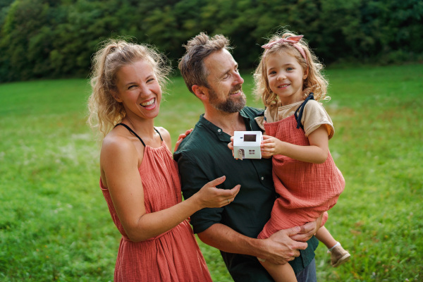 Little girl with her parents holding paper model of house with the solar panels.Alternative energy, saving resources and sustainable lifestyle concept.