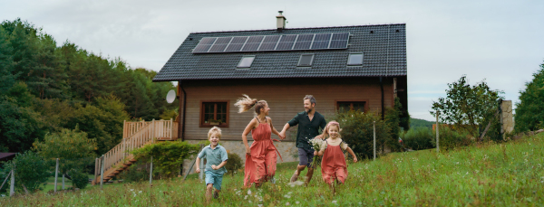 Happy family running near their house with a solar panels. Alternative energy, saving resources and sustainable lifestyle concept.