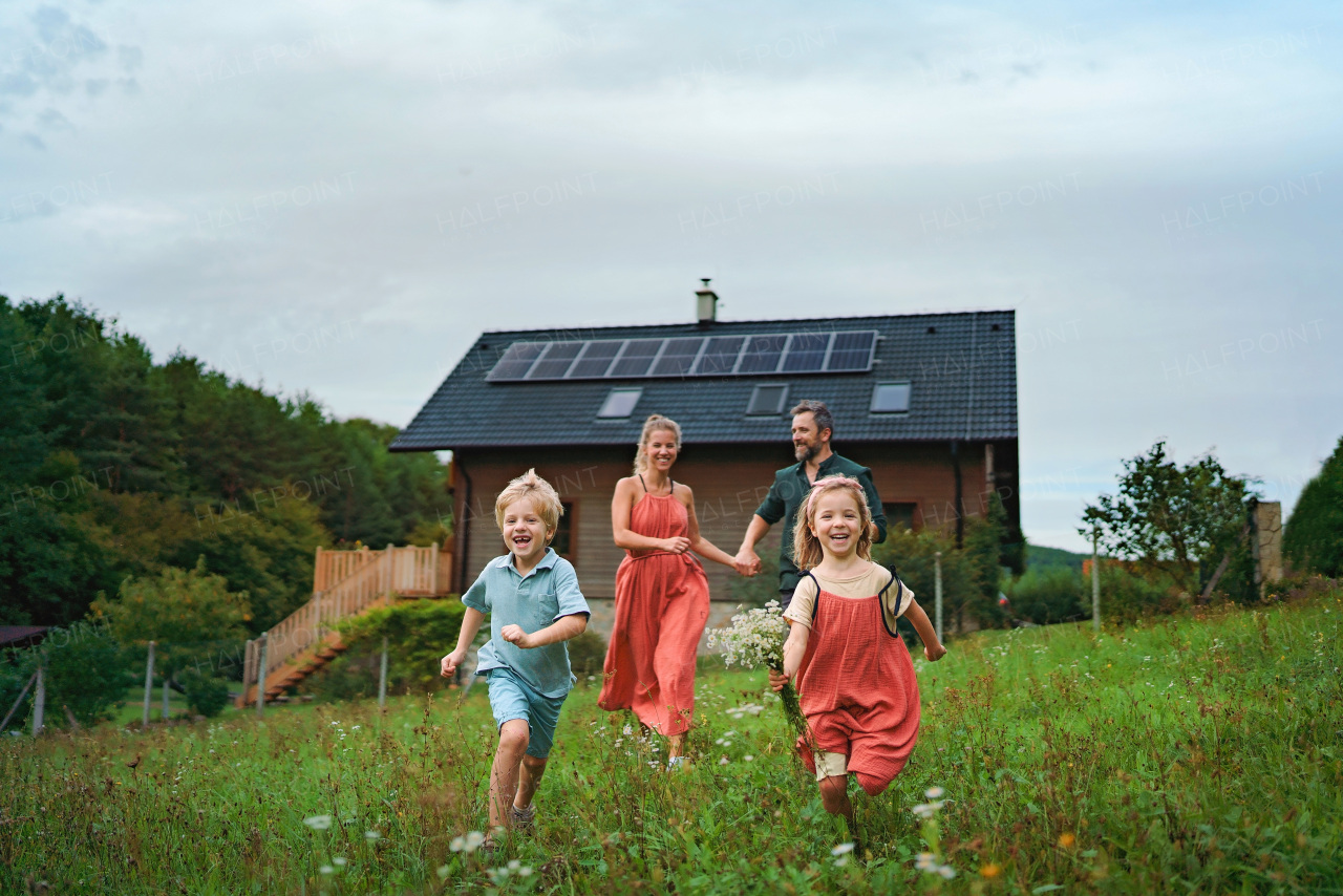 Happy family running near their house with a solar panels. Alternative energy, saving resources and sustainable lifestyle concept.