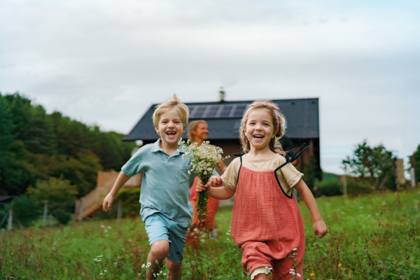 Happy family running near their house with a solar panels. Alternative energy, saving resources and sustainable lifestyle concept.