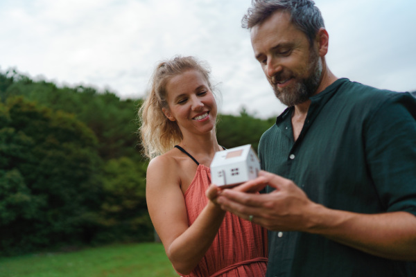 Close-up of happy couple holding paper model of house with solar panels, looking and dreaming about future. Alternative energy, saving resources and sustainable lifestyle concept.