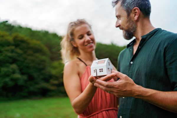 Close-up of happy couple holding paper model of house with solar panels, looking and dreaming about future. Alternative energy, saving resources and sustainable lifestyle concept.