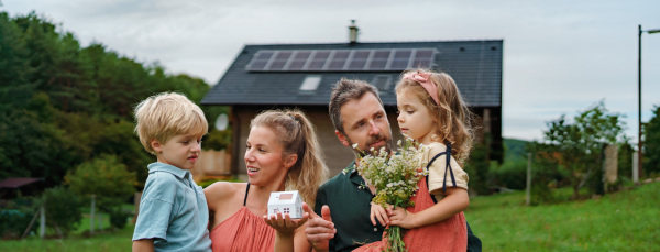 Close up of young family holding paper model of house with the solar panels.Alternative energy, saving resources and sustainable lifestyle concept.