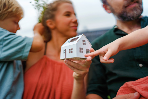 Close up of young mother holding paper model of house with the solar panels.Alternative energy, saving resources and sustainable lifestyle concept.