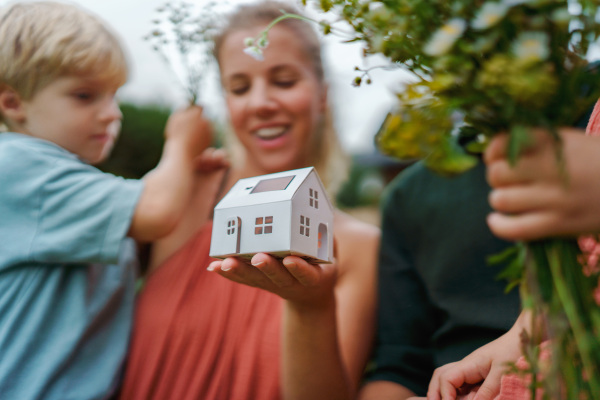 Close up of young mother holding paper model of house with the solar panels.Alternative energy, saving resources and sustainable lifestyle concept.