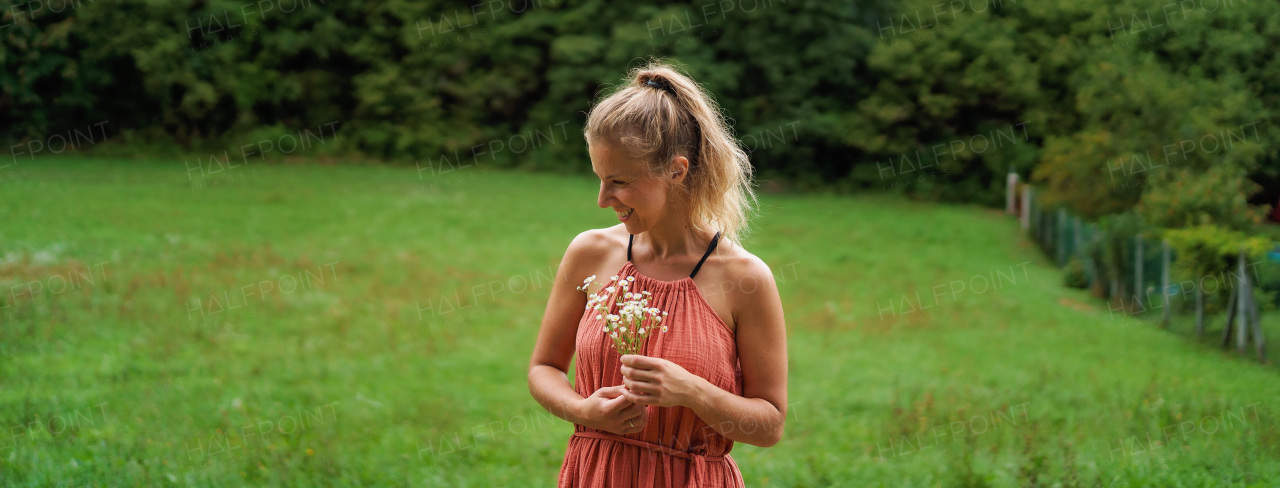 Happy woman in summer dress picking flowers at meadow.