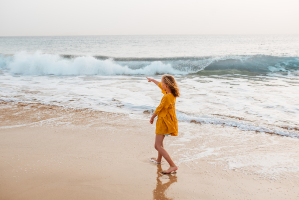 Young girl on the beach. Rear view of blonde girl enjoying sandy beach, looking at crystalline sea in Canary Islands. Concept of beach summer vacation with kids.