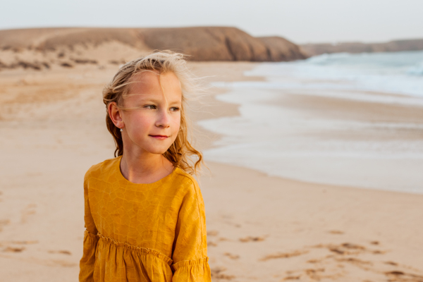 Young girl on the beach. Smilling blonde girl enjoying sandy beach, looking at crystalline sea in Canary Islands. Concept of beach summer vacation with kids.