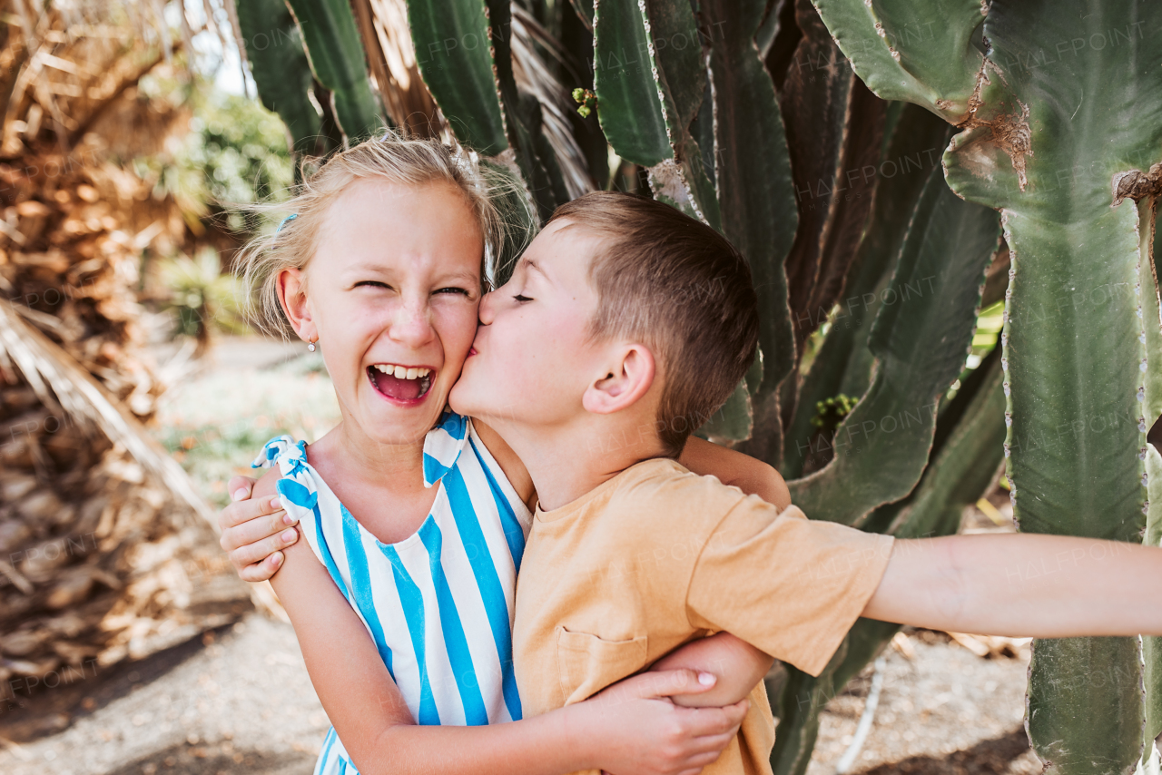 Portrait of siblings on summer vacation in holiday destination. Happy brother kissing sister on cheek. Concept of a family beach summer vacation with kids.