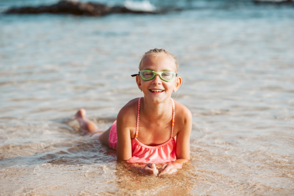 Young girl on the beach. Smilling blonde girl enjoying sandy beach, looking at crystalline sea in Canary Islands. Concept of beach summer vacation with kids.