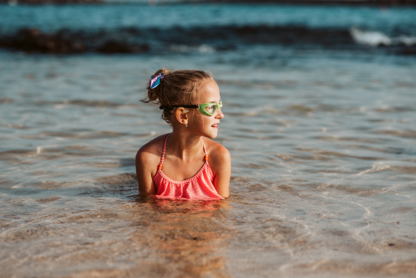 Young girl on the beach. Smilling blonde girl enjoying sandy beach, looking at crystalline sea in Canary Islands. Concept of beach summer vacation with kids.