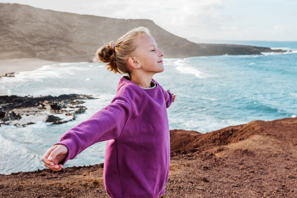 Young girl with closed eyes enjoing sea wind blowing in face. Beautiful blonde girl enjoying nature of Canary islands. Concept of beach summer vacation with kids.