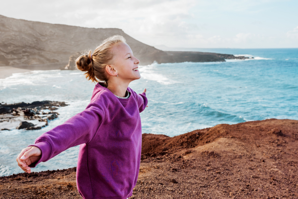 Young girl with closed eyes enjoing sea wind blowing in face. Beautiful blonde girl enjoying nature of Canary islands. Concept of beach summer vacation with kids.