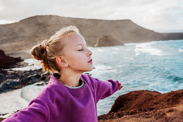 Young girl with closed eyes enjoing sea wind blowing in face. Beautiful blonde girl enjoying nature of Canary islands. Concept of beach summer vacation with kids.