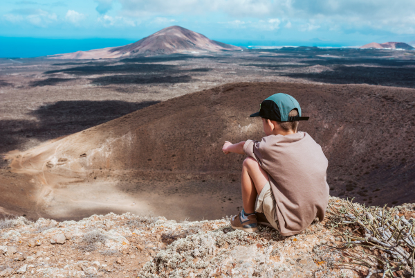 Boy sitting on top of hill. Family exploring new places during summer vacation on Canary islands, Lanzarote.