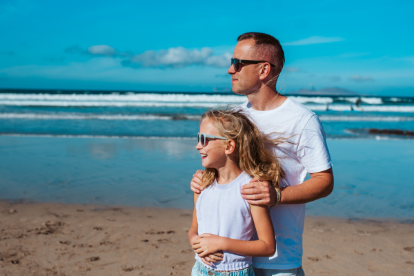 Father and daughter, standing on beach. Dad and girl enjoying sandy beach, looking at crystalline sea in Canary Islands. Concept of beach summer vacation with kids.