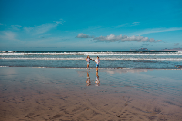 Siblings playing on beach, running, skipping in water. Smilling girl and boy on sandy beach of Canary islands. Concept of a family beach summer vacation with kids.