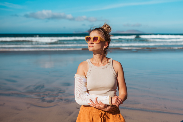 Beautiful woman with broken arm on beach. Arm cast, injured during family vacation in holiday resort. Concept of beach summer vacation.