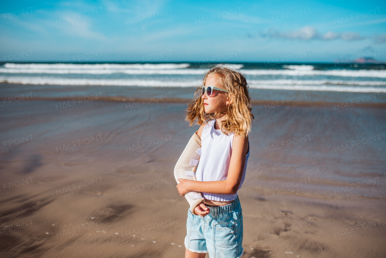 Girl with broken arm on beach. Young blonde girl has arm cast, injured during family vacation in holiday resort. Concept of a beach summer vacation with kids.