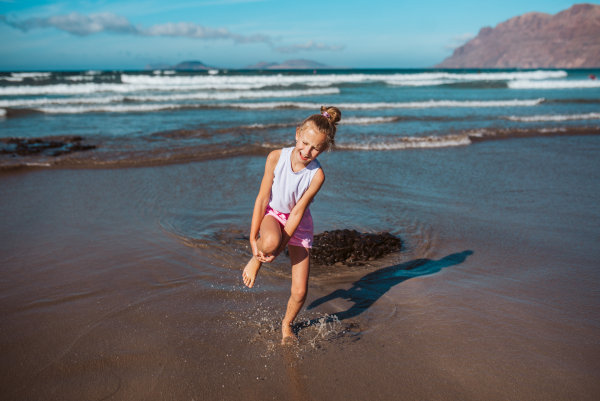 Girl injured her leg on beach. Blonde girl in pain on sandy beach, healthcare problems at vacation. Concept of beach summer vacation with kids.