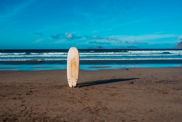 Surfboard stucked in sand on a sunny beach during sunset.