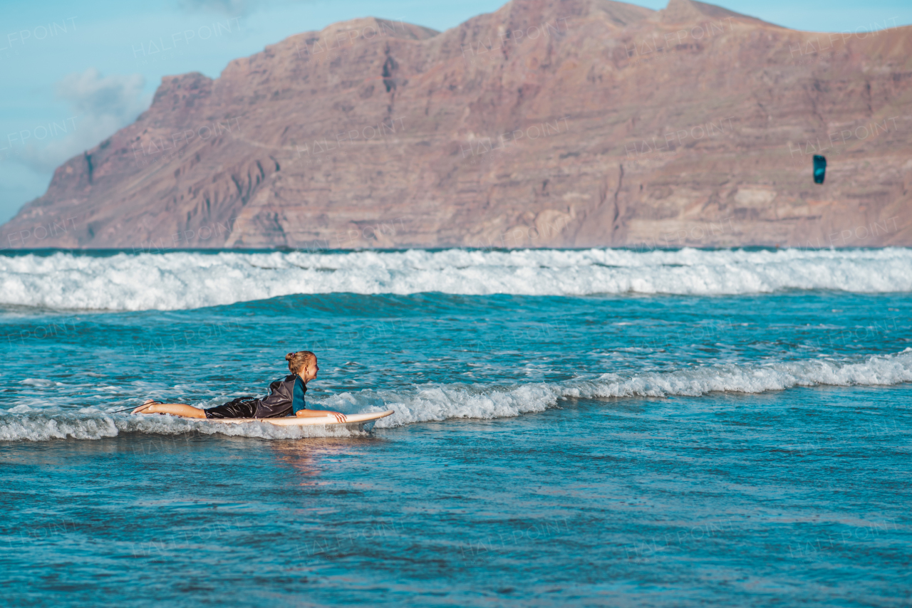 Young boy surfing in sea waves. Smilling boy in neoprene wetsuit lying on sufrboard. Concept of popular water sport for kids.