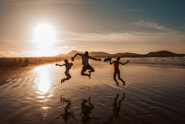 Jumping family on beach. Father and two kids enjoying sandy beach during sunset in Canary Islands. Concept of beach summer vacation with kids.