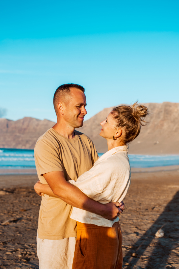 Beautiful couple embracing on sand beach. Celebrating anniversary on vacation, honeymoon for mature couple. Concept of romantic beach vacation.