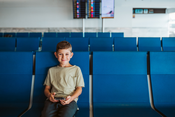 Boy sitting in empty airport of vacation destination, excited about the sea and the beach. Family summer holidays.