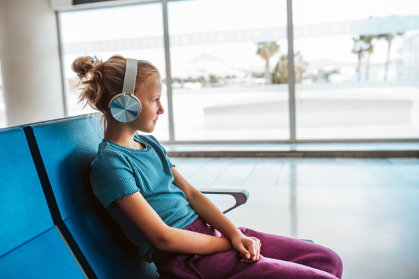 Girl with headphones sitting in empty airport of vacation destination, excited about the sea and the beach. Family summer holidays.