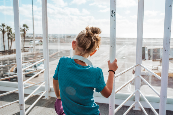 Girl looking through the airport window at the vacation destination, excited about the sea and the beach.