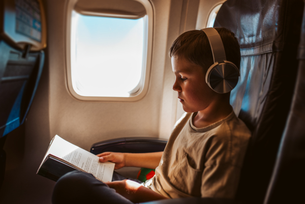 Boy with headphones on reading book in airplane. Concept of a famiily beach summer vacation with kids.