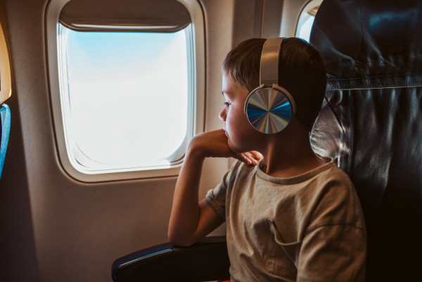 Boy with headphones sitting airplane, looking out of window. Concept of a famiily beach summer vacation with kids.