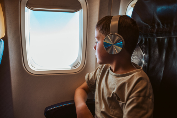 Boy with headphones on is looking out the airplane window. Concept of a famiily beach summer vacation with kids.