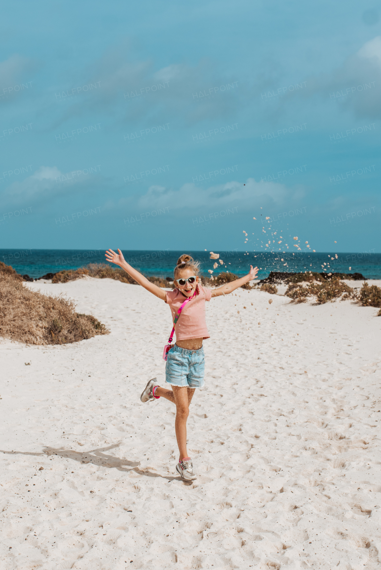 Girl throwing sand jumping, standing on beach. Family summer vacation by the sea.