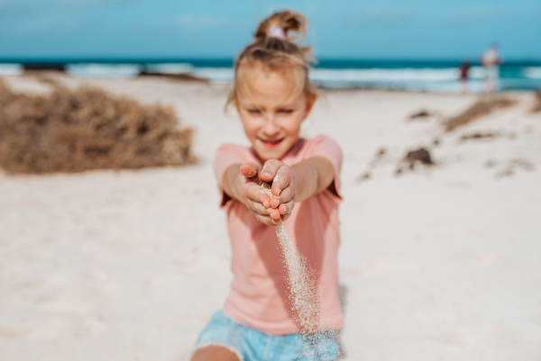 Girl with sand falling from his clnched fist, standing on beach. Family summer vacation by the sea.